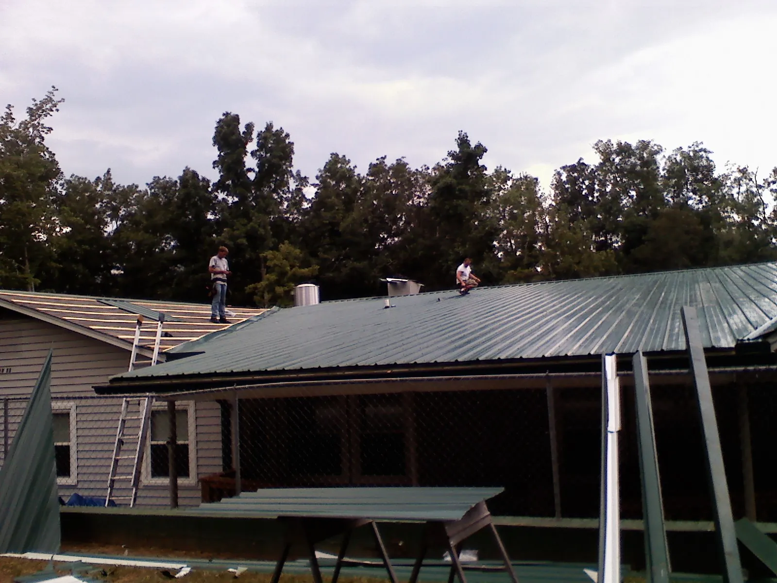 Two roofers installing green metal panels above a covered porch in Nelson